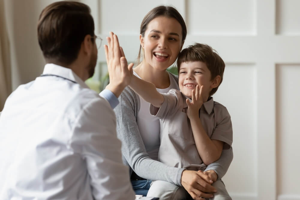 Mutter und Kind geben einem Arzt ein High-Five, lächelnd im Gespräch.