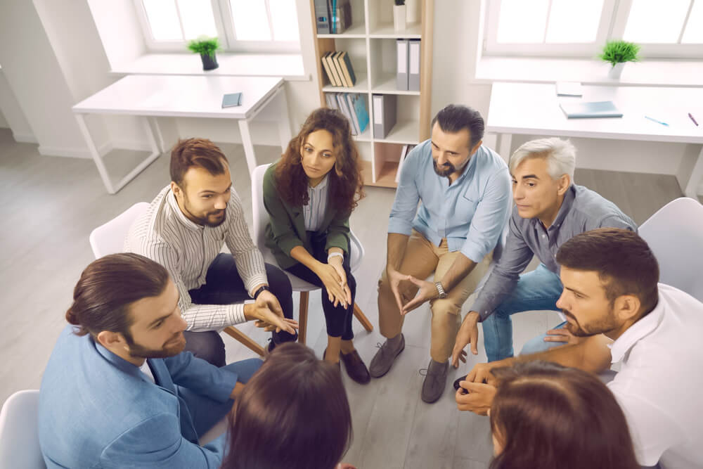 Team sitzt im Stuhlkreis und diskutiert gemeinsam.